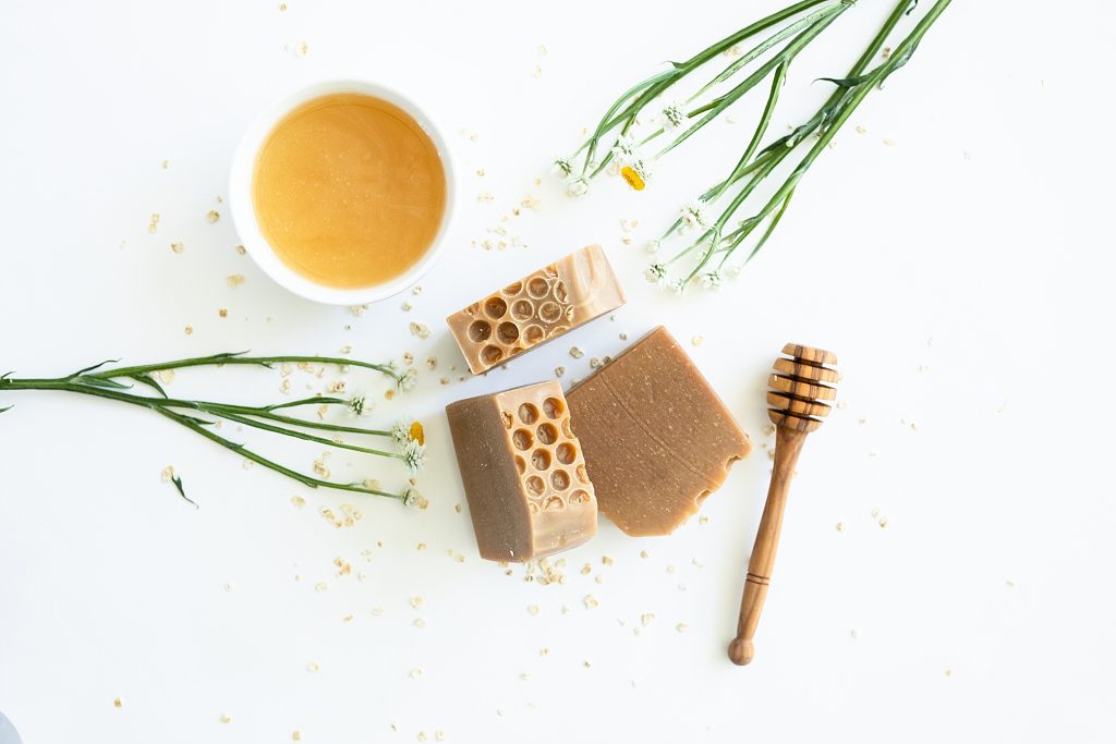 Flatlay image of soap with honey and flowers nearby, sprnink oatmeal (ingredients in soap)