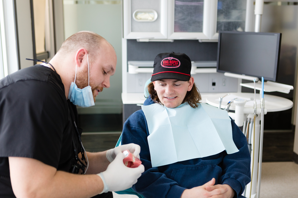 Lethbridge dentist photography showing Cole Nelson talking with client and showing him teeth models