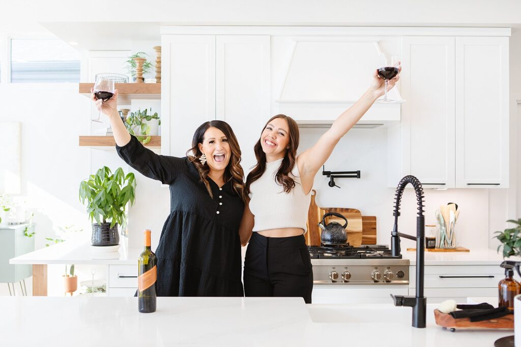 Two women celebrating with glasses of wine in a kitchen they designed. Lethbridge brand photography by Kinsey Holt